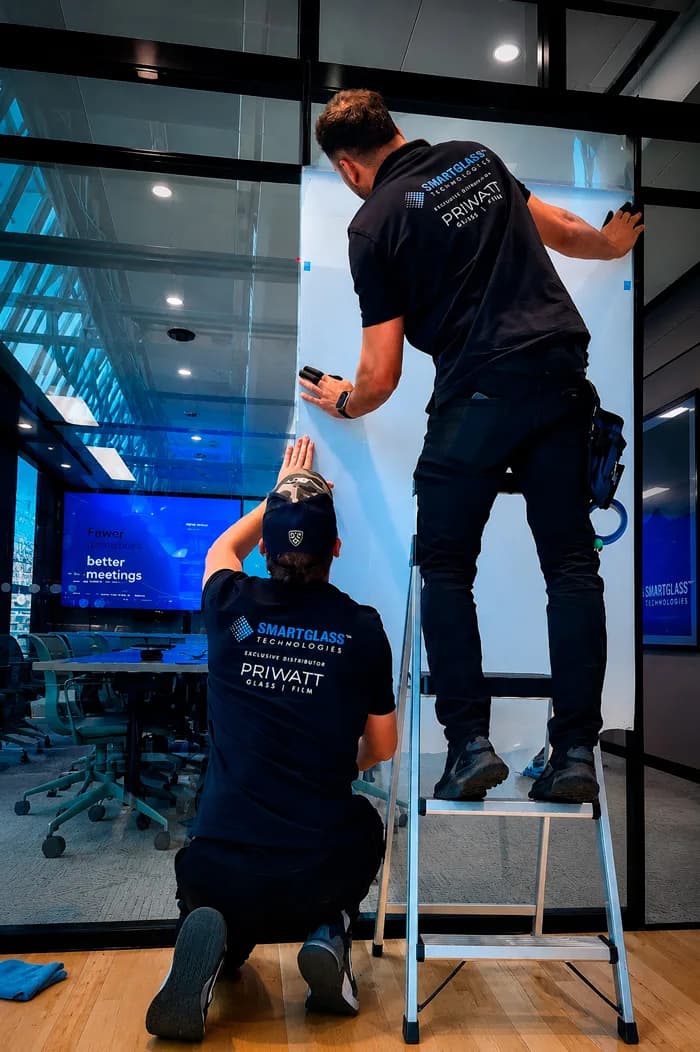 Two PriWatt fitters applying smart film to a glass office partition