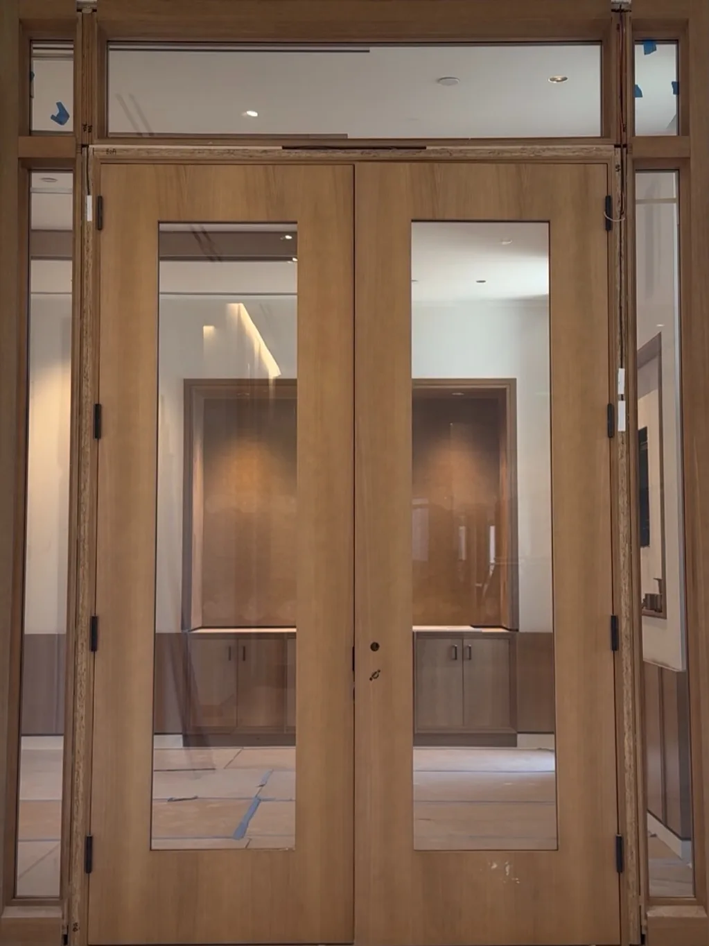 An interior double door glazed with PriWatt reverse switchable glass, clear — a lit room, a joinery niche and cabinets visible through both leaves